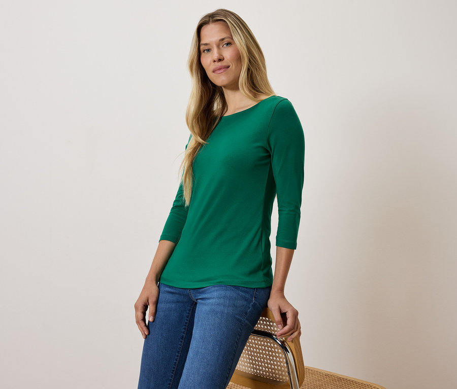 Blonde en T-shirt vert à manches trois-quarts et jean bleu assise sur une chaise.