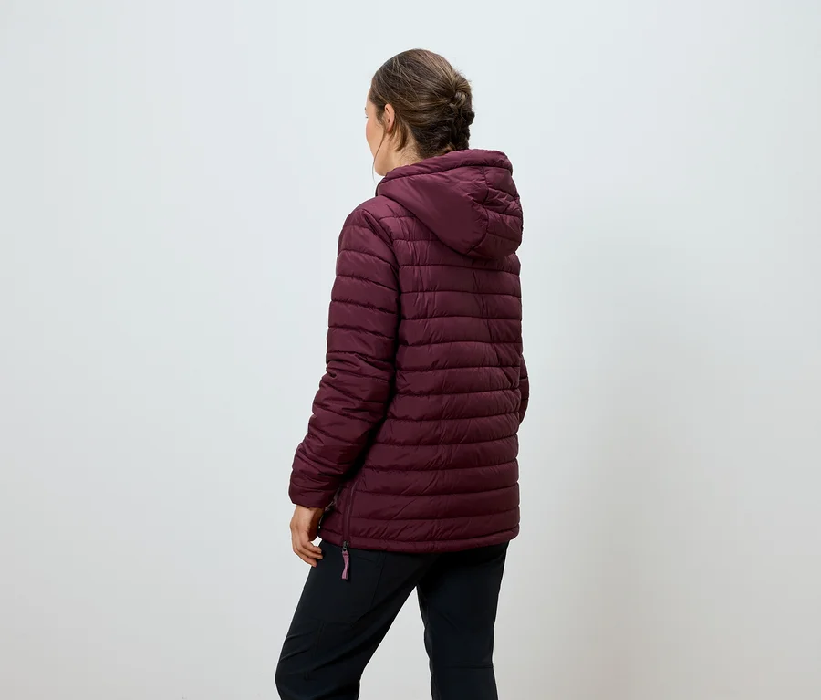 Une femme se tient dos à la caméra et porte une veste matelassée bordeaux avec capuche et un pantalon noir.