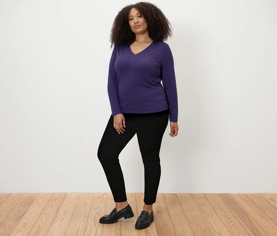 Une femme pose, portant un t-shirt structuré à manches longues prune et un jegging.