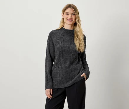 Une femme pose en pull gris en maille et pantalon noir.