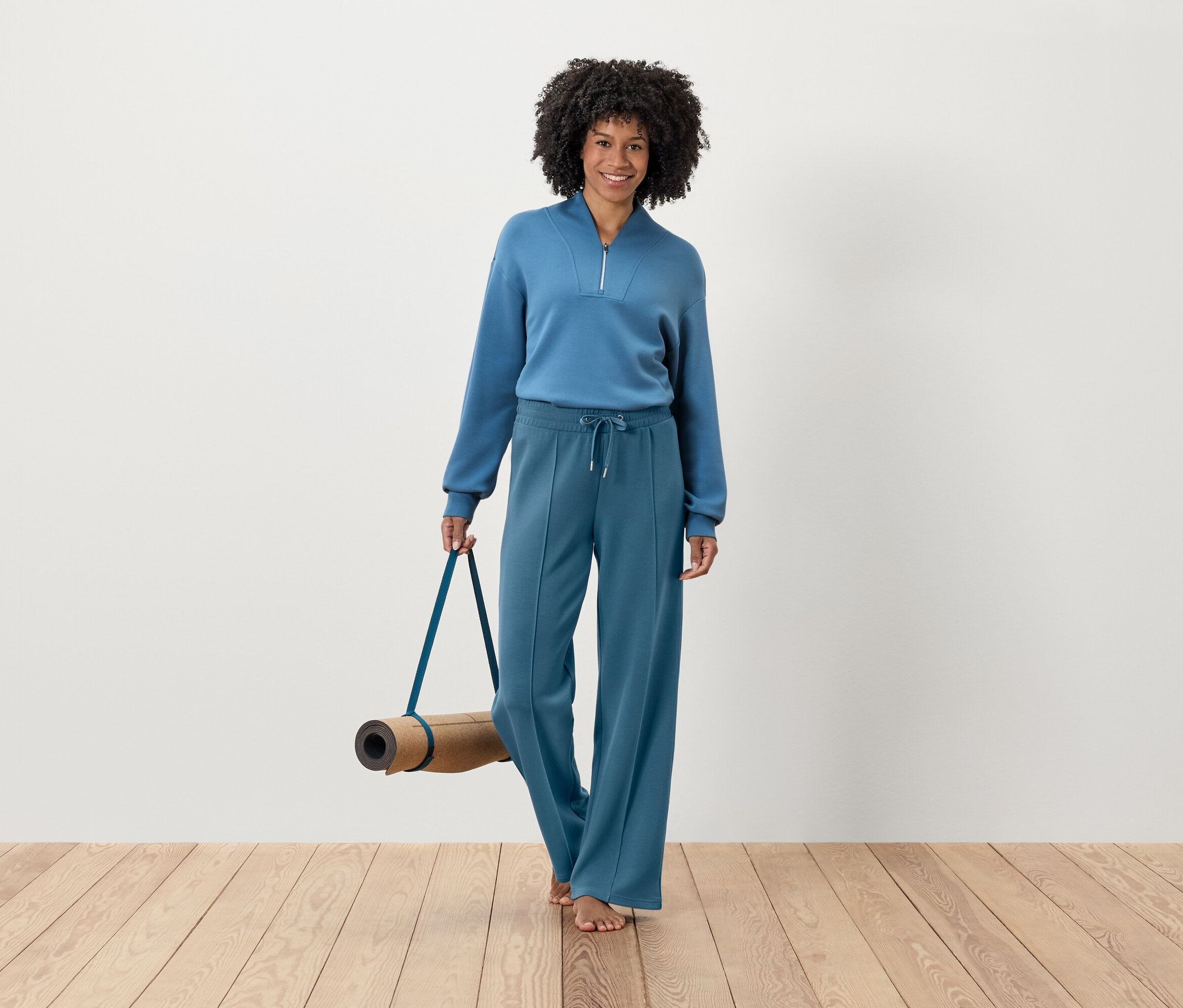 Femme en survêtement bleu tenant un tapis de yoga.