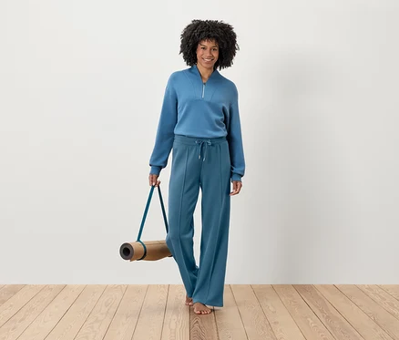 Femme en survêtement bleu tenant un tapis de yoga.
