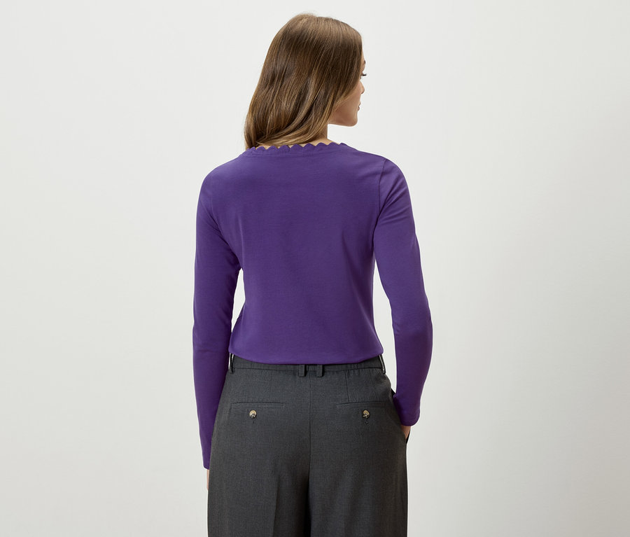 Une femme, dos à la caméra, porte un t-shirt violet à manches longues et un pantalon gris.