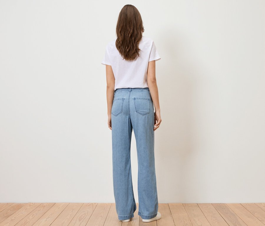 Vue de dos d'une femme aux longs cheveux bruns portant un t-shirt blanc et un jean bleu clair.