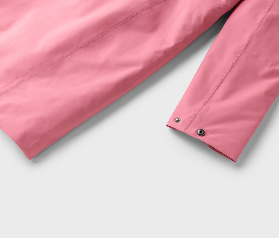 Gros plan sur la manche rose d'une veste avec des boutons-pression argentés sur un fond gris clair.