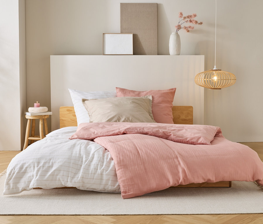 Un lit avec une couette rose, des draps blancs et des oreillers beiges se trouve sur un tapis dans une chambre.