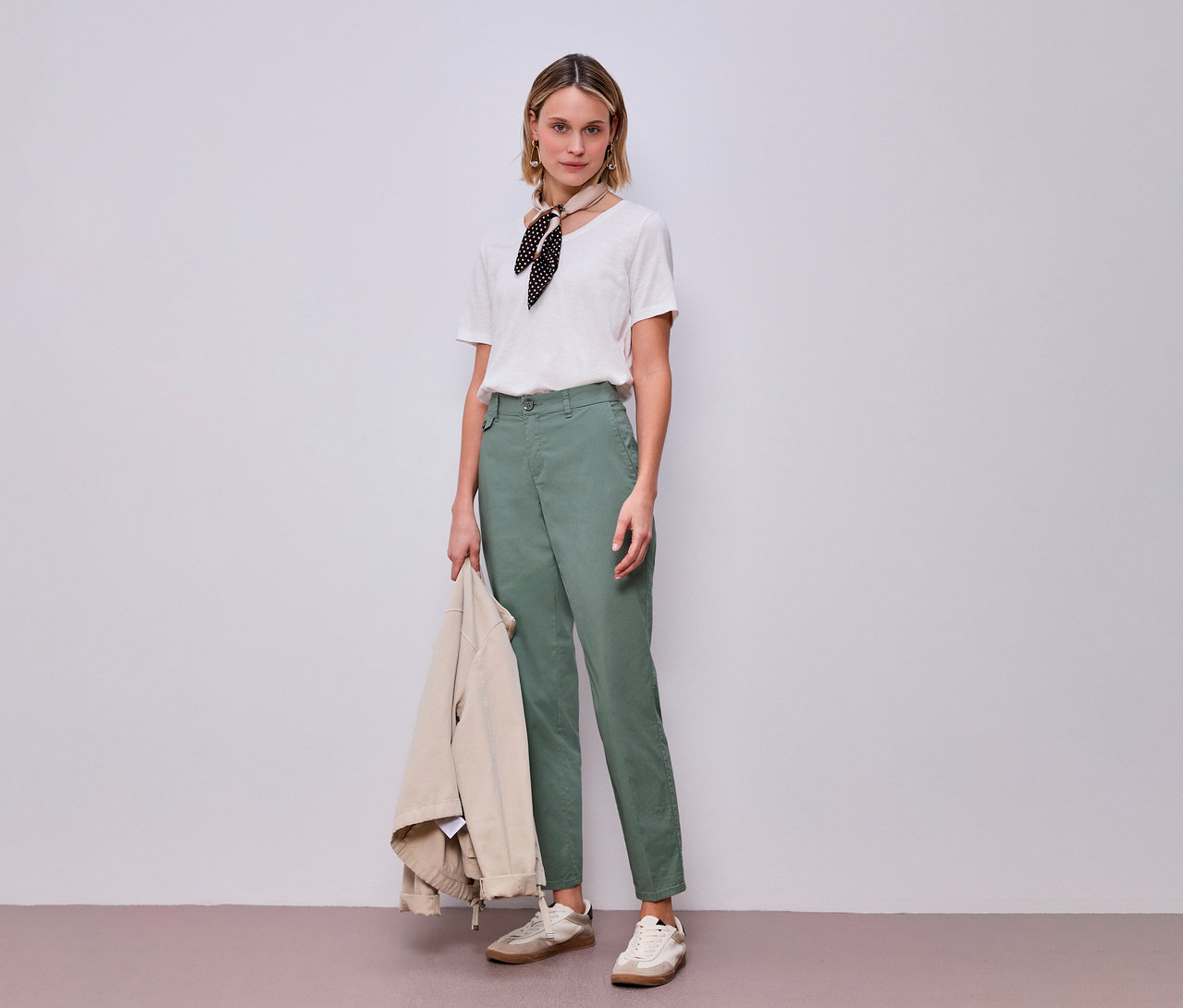 Femme portant un chino Street One menthe avec un t-shirt et un foulard, tenant une veste.