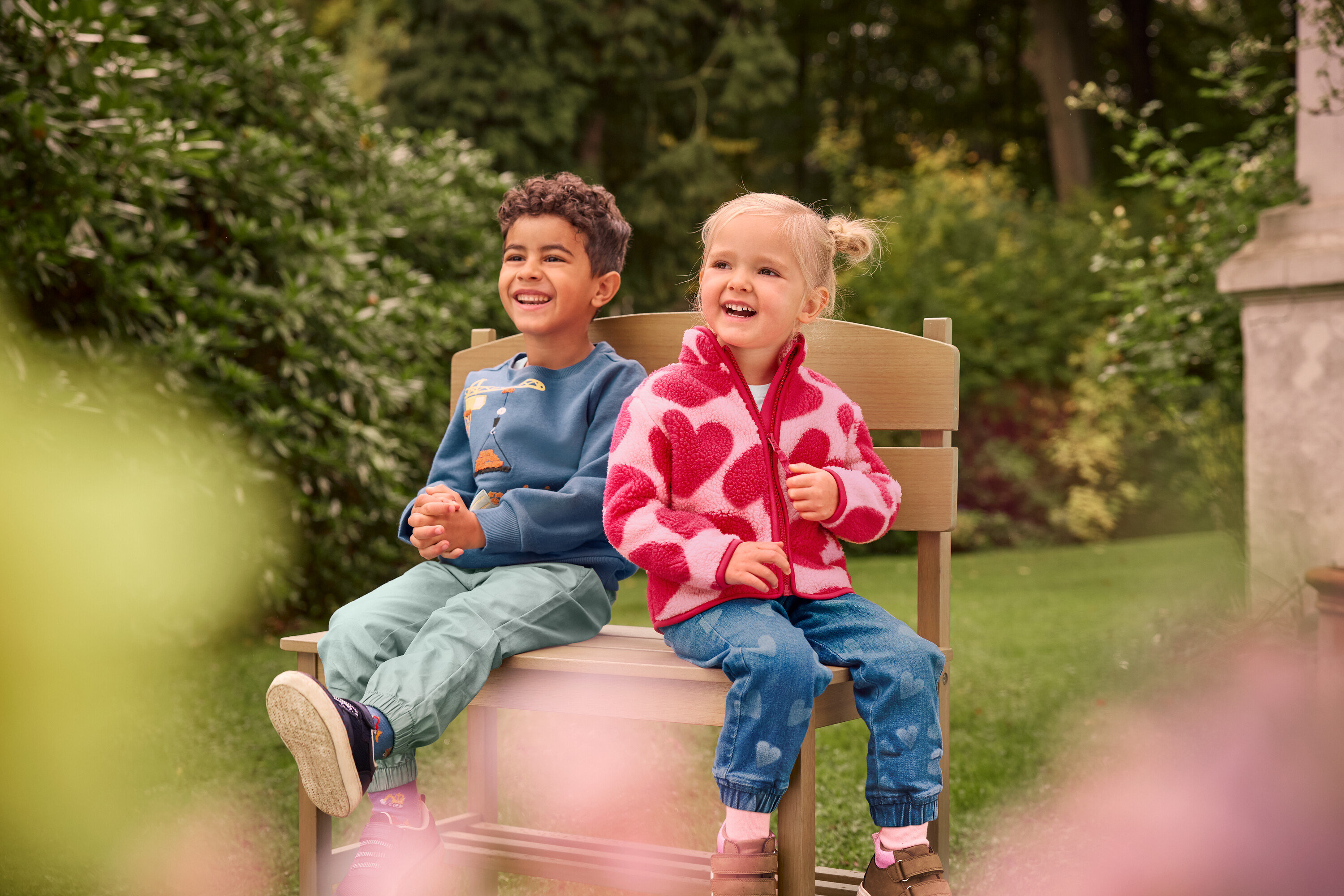 Un garçon et une fille sont assis et rient sur un petit banc de jardin avec rangement.