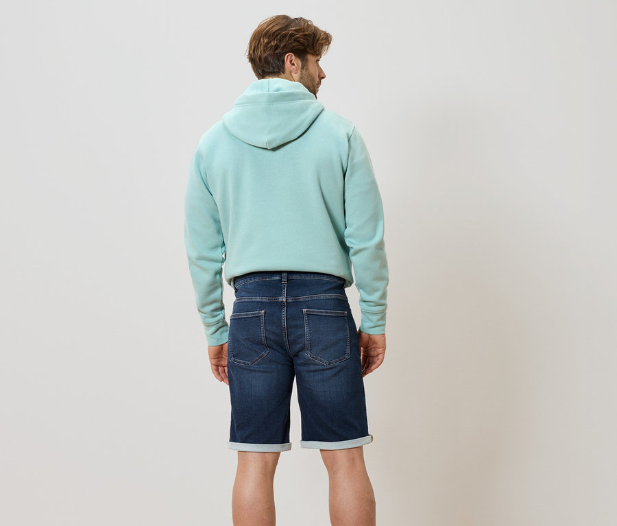 Vue de dos d'un homme portant un sweat à capuche bleu clair et un short en jean.