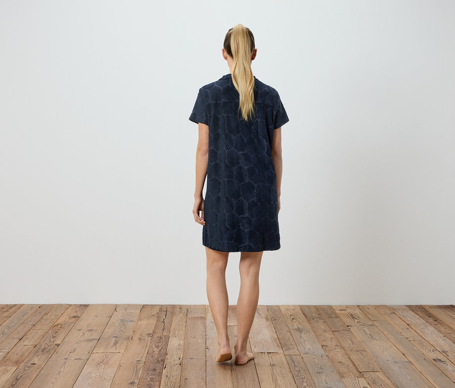 Une femme se tient dos à la caméra, portant une robe bleu foncé à motifs.