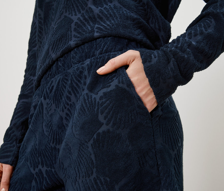 Femme glissant sa main dans la poche d'un pantalon bleu marine à motif de feuilles, avec un haut assorti.