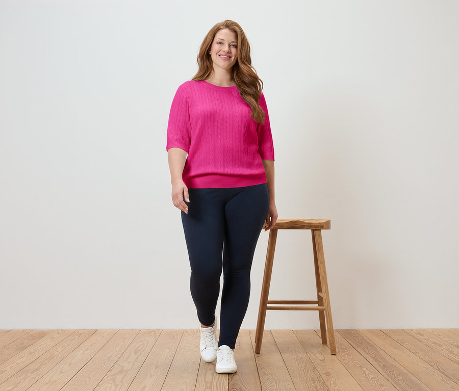 Femme marchant sur un plancher en bois, portant un haut rose et un legging bleu marine