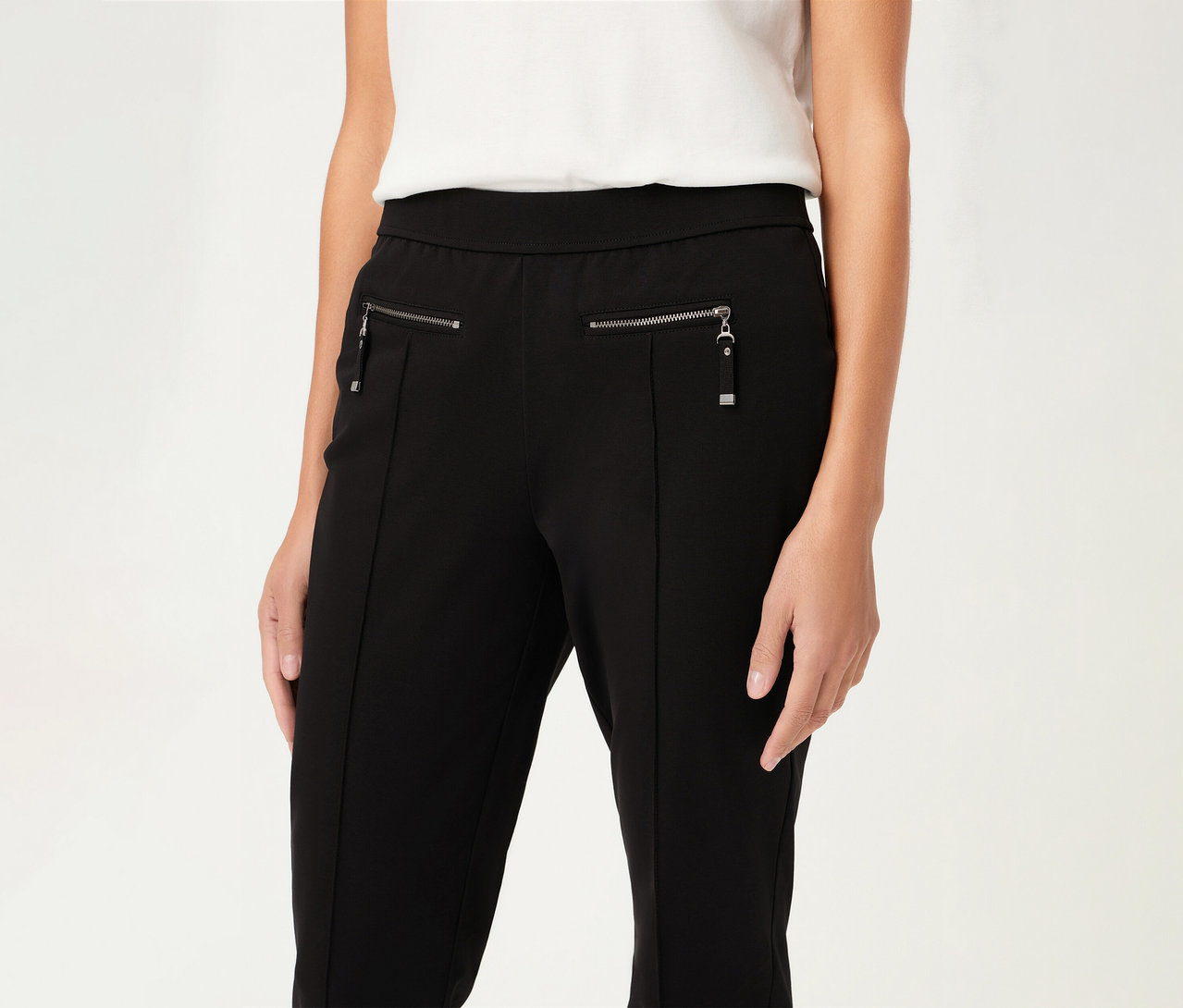 Une femme porte un pantalon Olsen, slim, noir avec des fermetures éclair et un haut blanc.