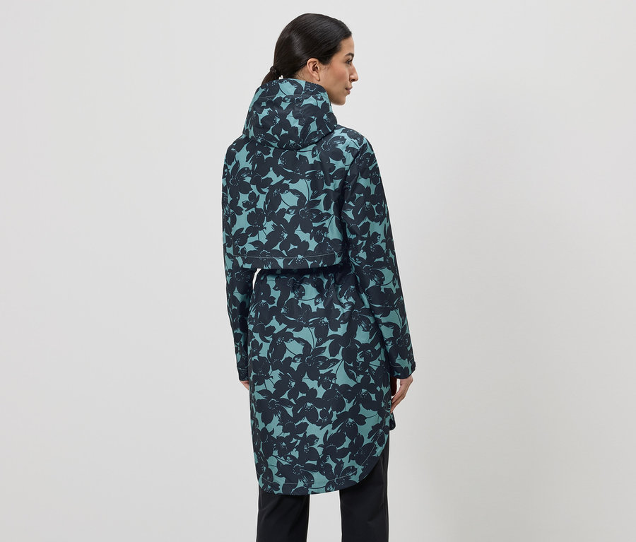 Femme vue de dos, portant un long imperméable bleu-vert à capuche avec un motif floral noir et un pantalon noir.