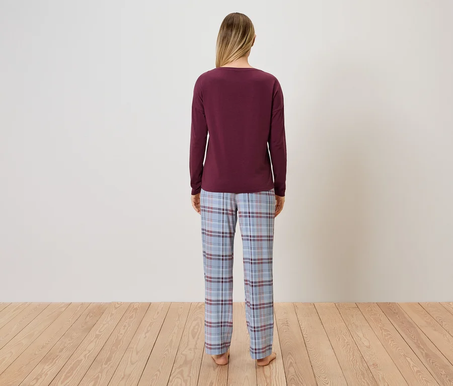 Une femme, vue de dos, porte un pull bordeaux et un pantalon de pyjama à carreaux bleus.