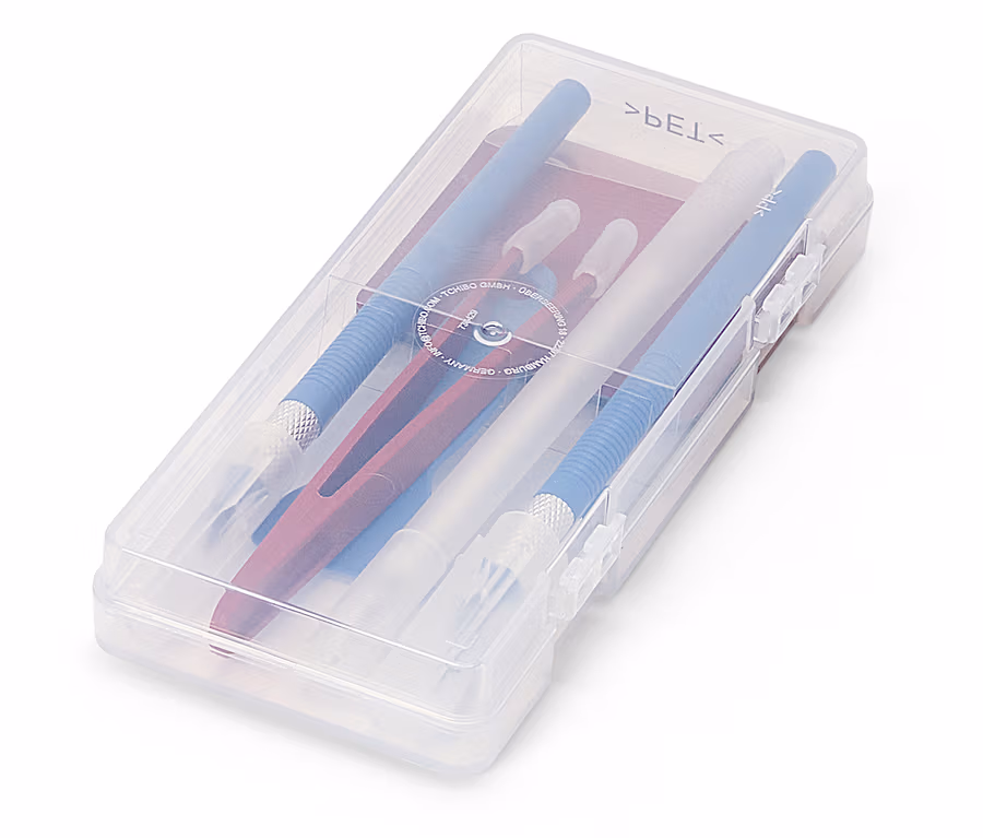 Un récipient transparent contenant des couteaux d'artisanat bleus, blancs et rouges, chacun avec des capuchons de protection.