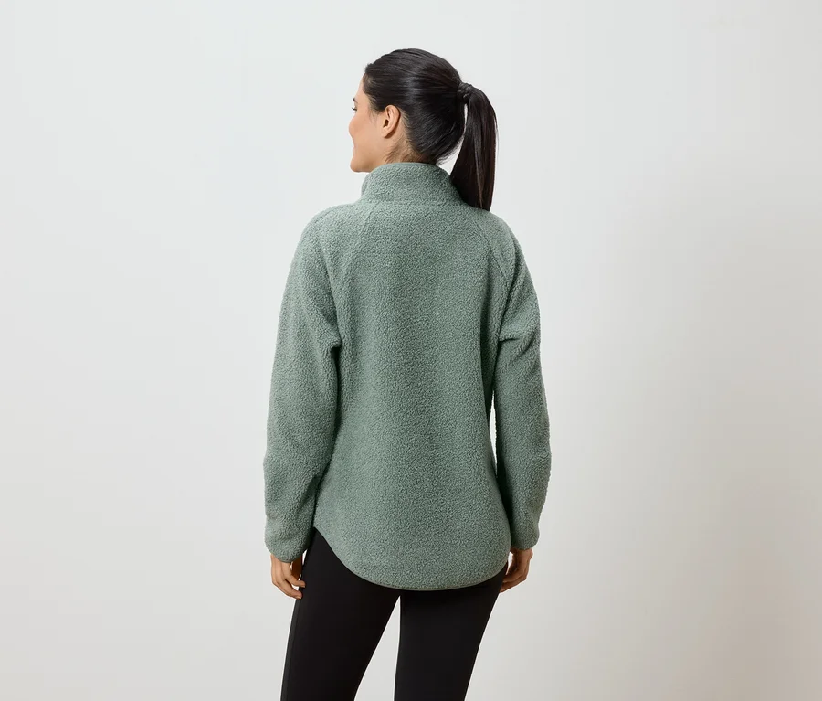 Une femme avec une queue de cheval porte un pull en polaire vert menthe et un legging noir, vue de dos.