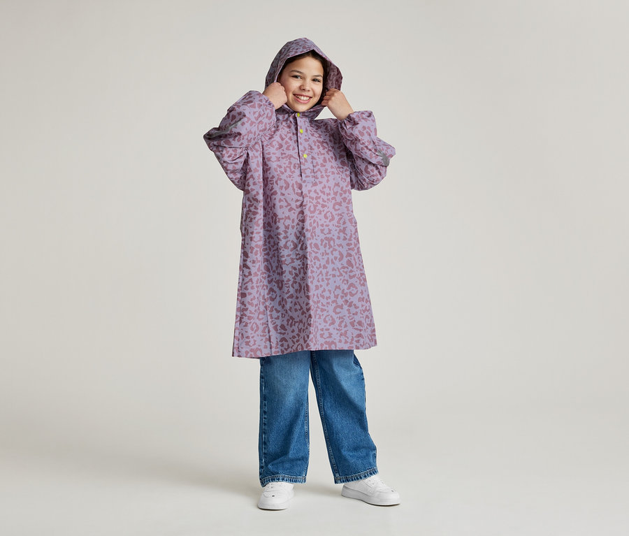 Une jeune fille souriante à capuche porte un imperméable violet à motif léopard et un jean bleu.
