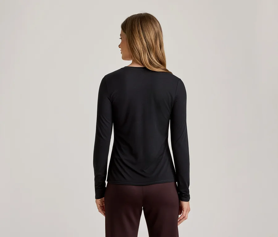 Vue arrière d'une femme aux longs cheveux blonds portant un haut noir à manches longues et un pantalon bordeaux.