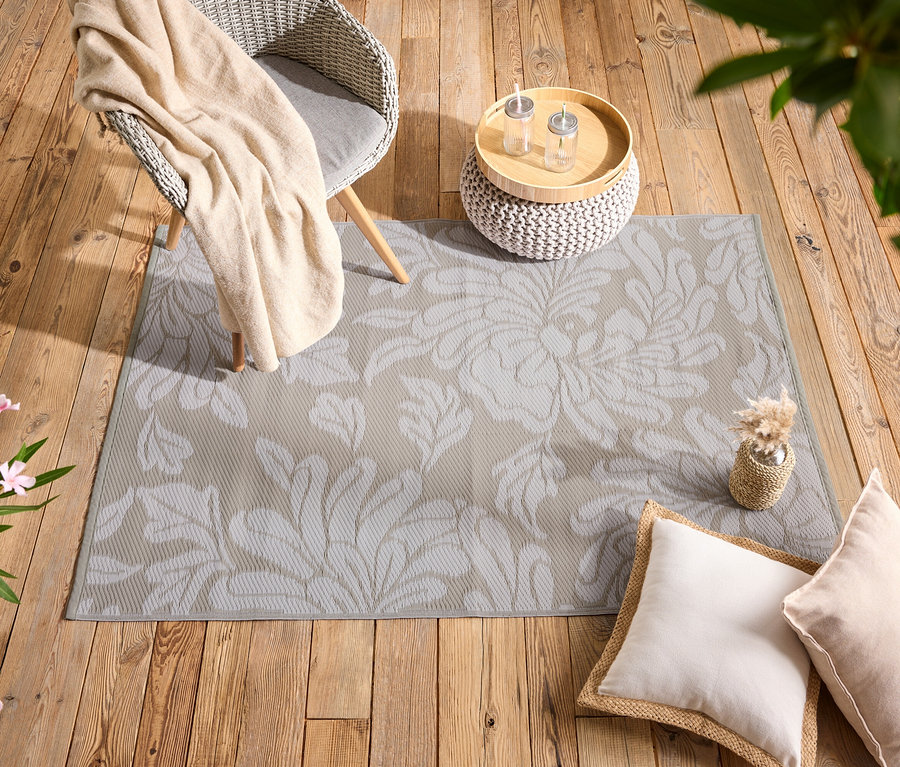 Un tapis beige à motifs floraux repose sur un plancher en bois, à côté de coussins, une chaise et une table.