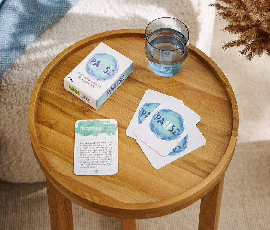 Sur une table ronde en bois se trouvent une boîte et des cartes portant l'inscription "PAUSE" ainsi qu'un verre d'eau.