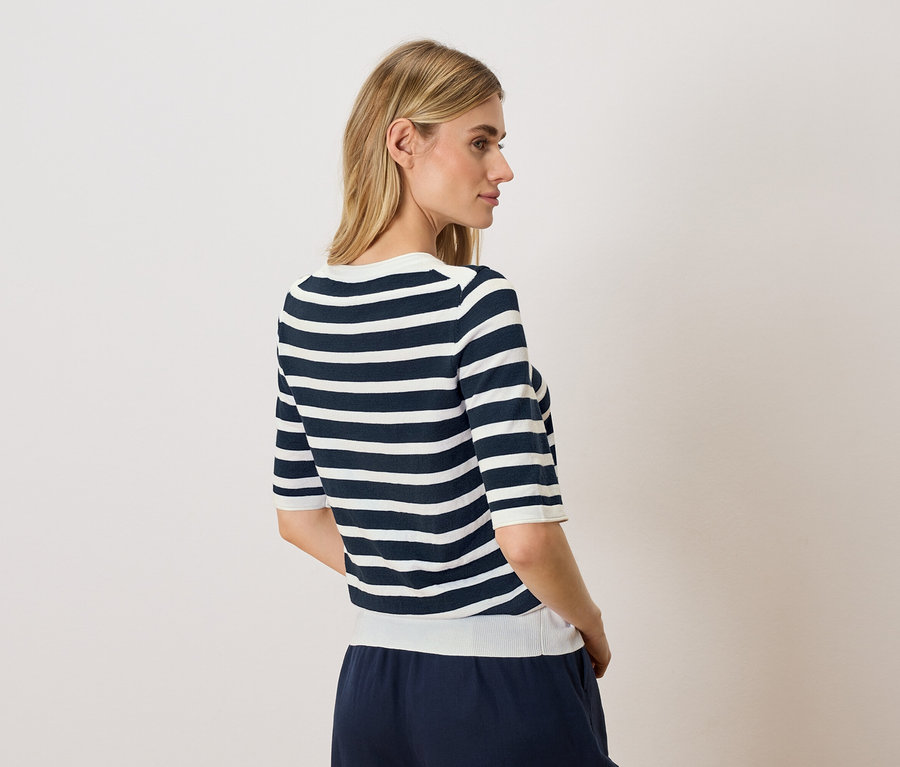 Une femme blonde porte un haut rayé à manches courtes et un pantalon bleu.