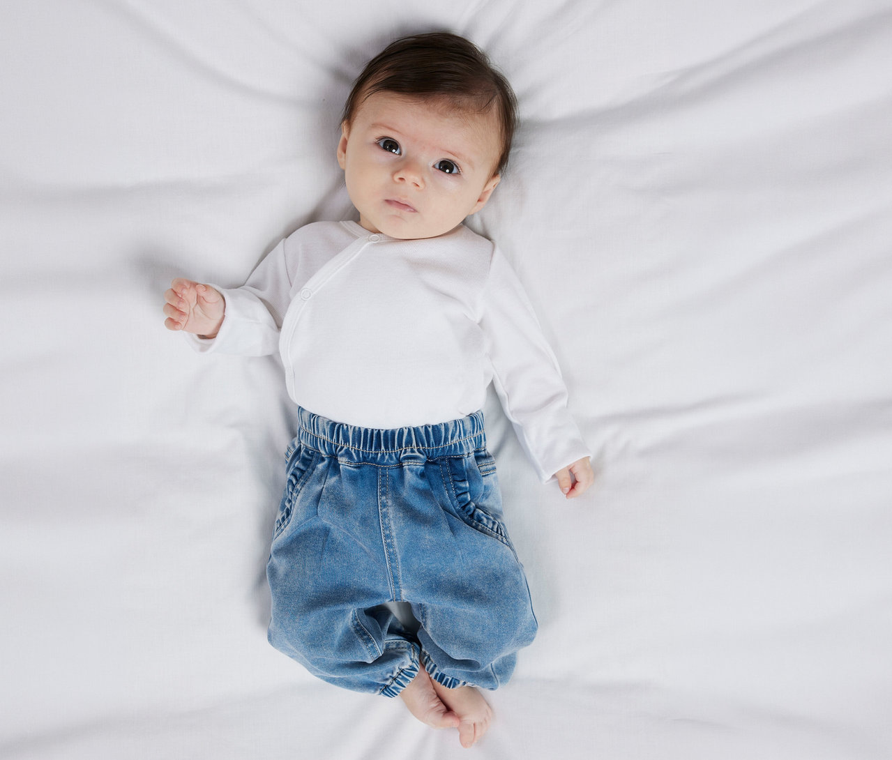 Un bébé est allongé sur le dos et porte un body blanc et un jean pour bébé NAME IT.