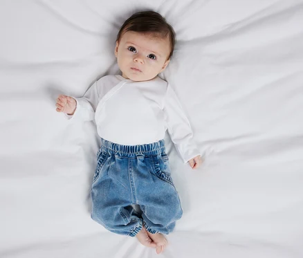 Un bébé est allongé sur le dos et porte un body blanc et un jean pour bébé NAME IT.