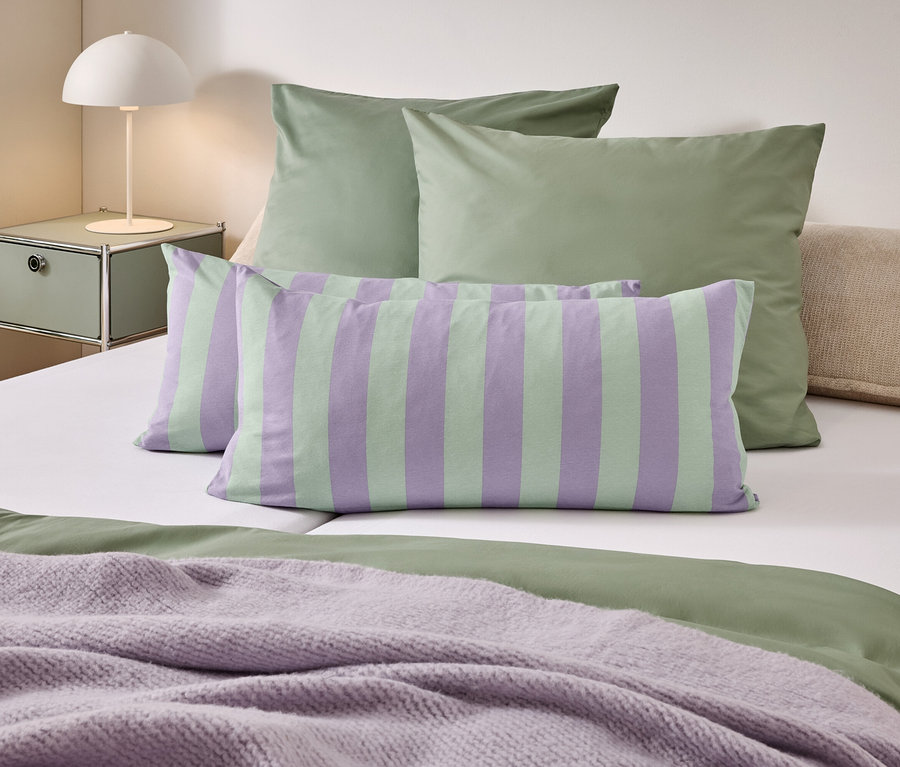 Un lit avec des draps verts, des oreillers rayés et une couverture violette.