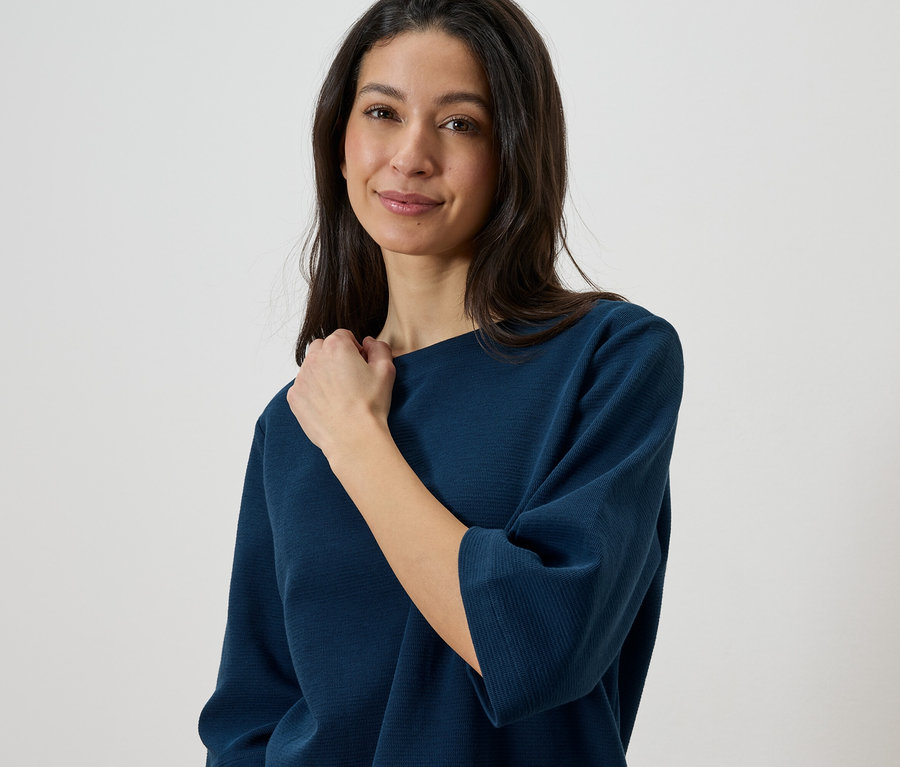 Femme portant un haut bleu texturé touchant son cou.