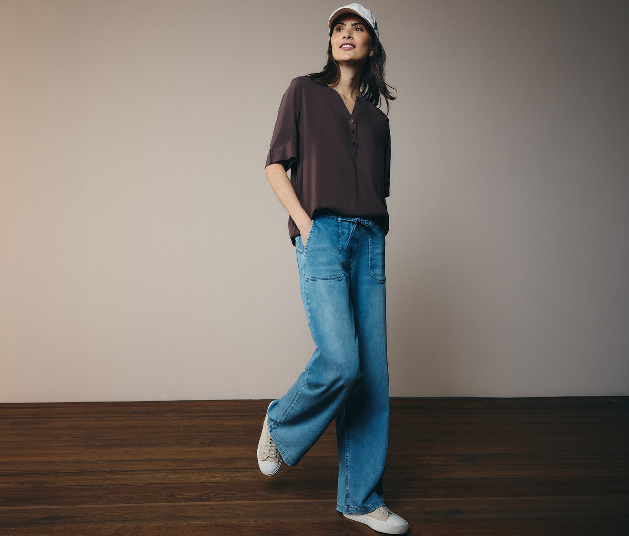 Femme portant une casquette de baseball et un chemisier tunique CECIL marron avec un jean et des baskets.