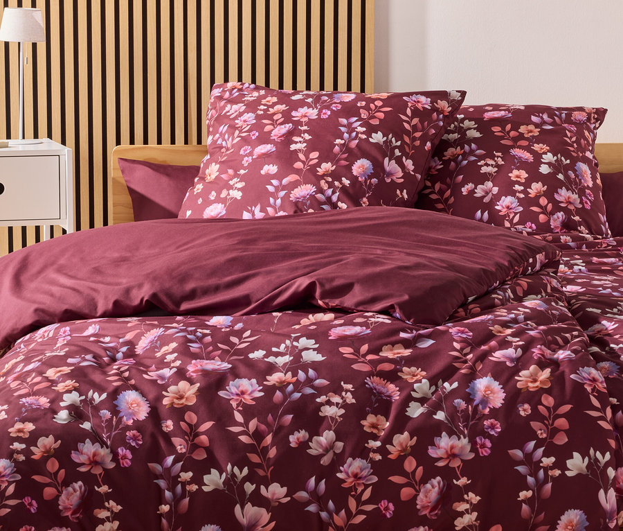 Une parure de lit bordeaux à motifs floraux est posée sur un lit avec une tête de lit en bois devant un mur avec des panneaux de bois.