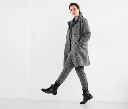 Femme posant en manteau gris, t-shirt à col bénitier, pantalon de jogging et mi-bas thermiques.