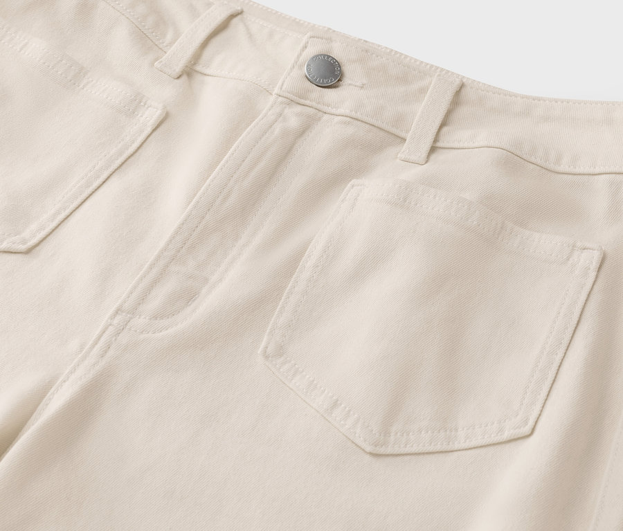 Gros plan d'un jean beige clair avec des poches et un bouton argenté.