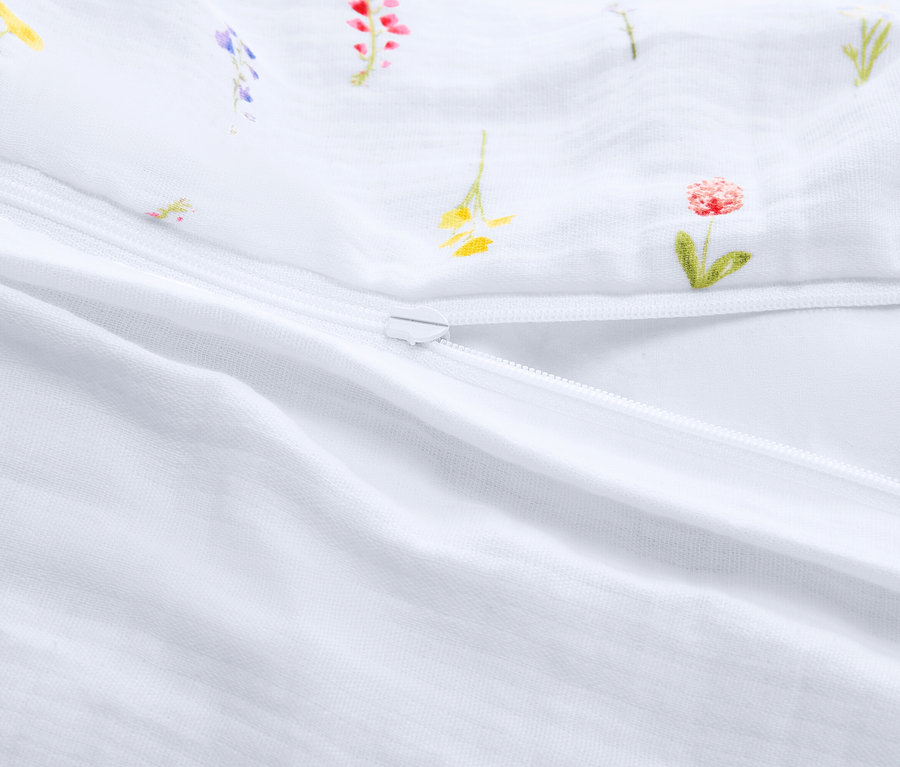 Vue détaillée d'un sac de couchage blanc partiellement ouvert avec une fermeture éclair et un motif floral.