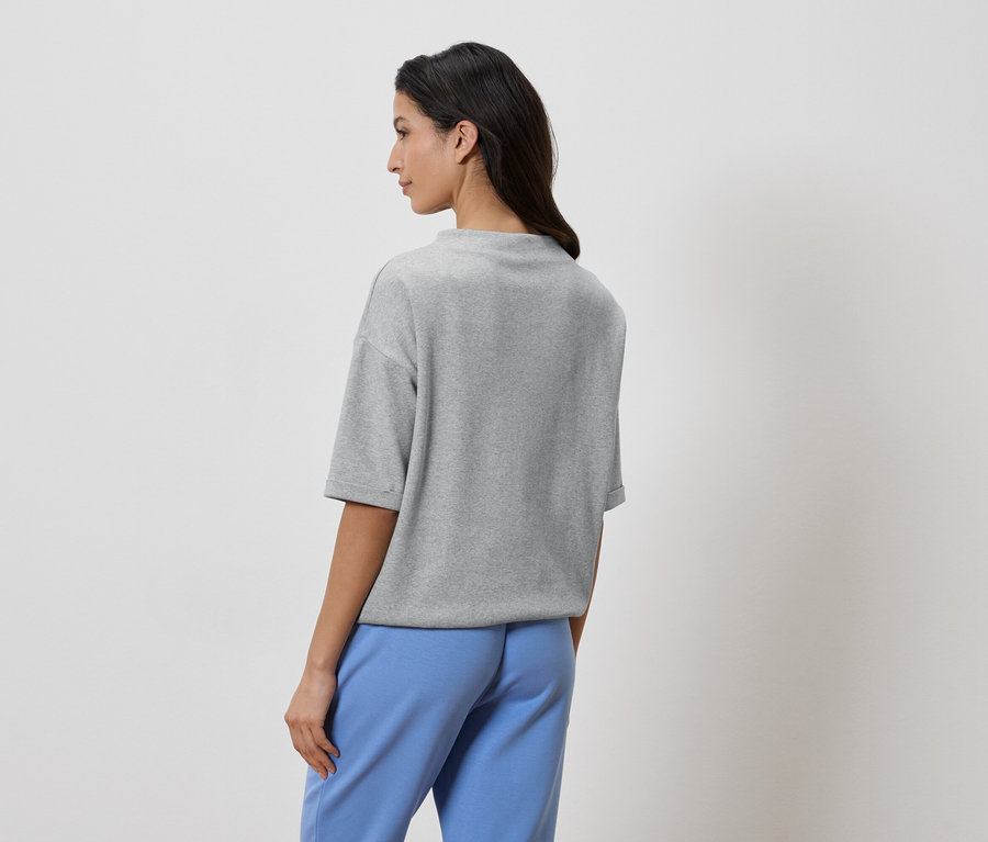 Femme vue de dos, portant un t-shirt gris et un pantalon bleu.