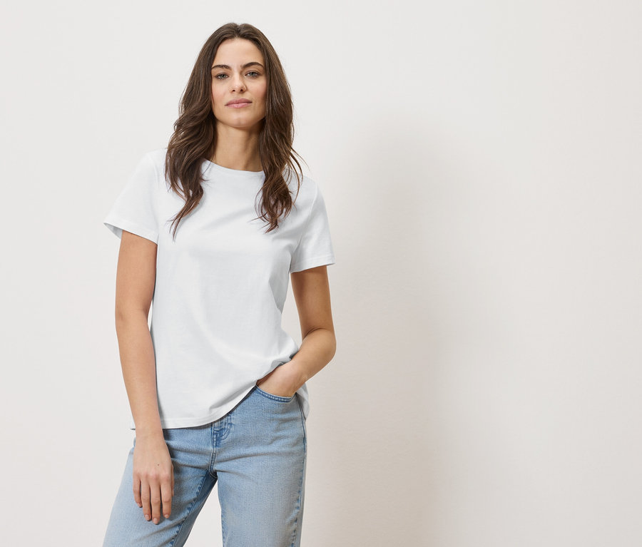 Femme aux cheveux bruns vêtue d'un t-shirt blanc et d'un jean