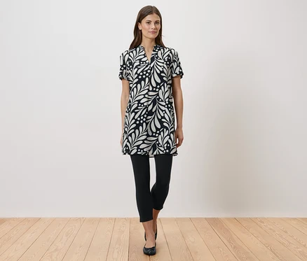 Femme debout portant une robe noire et blanche avec des leggings et des chaussures plates.