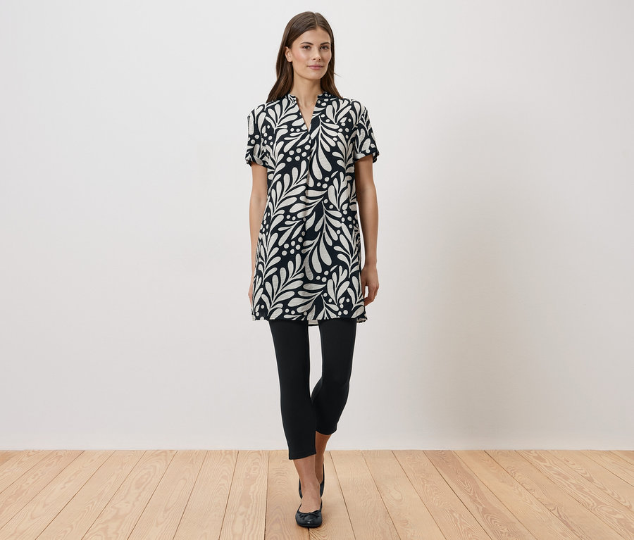 Femme debout portant une robe noire et blanche avec des leggings et des chaussures plates.