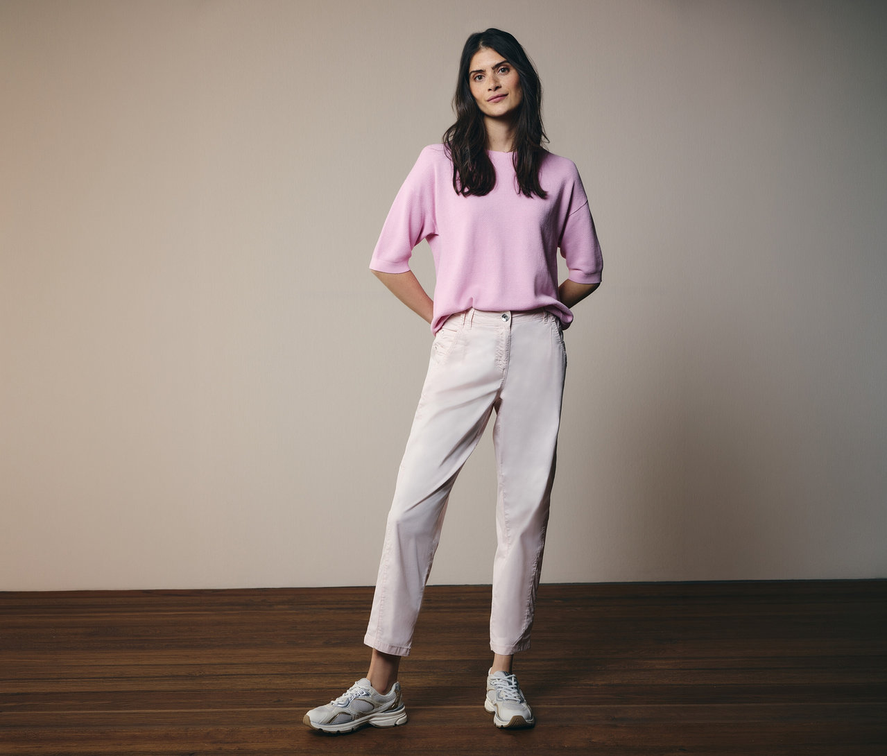 Femme portant un pull à manches courtes CECIL rose, un pantalon rose clair et des baskets, debout devant un fond clair.