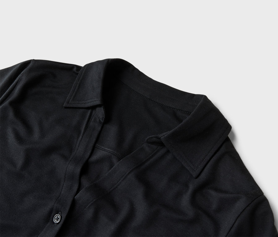 Gros plan d'une chemise noire avec col et patte de boutonnage sur un fond gris clair.