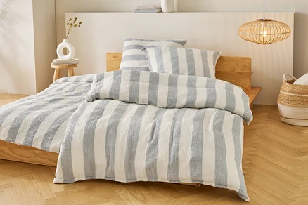 Lit avec des draps et des oreillers à rayures bleues et blanches sur un cadre de lit en bois. Une lampe est suspendue au-dessus du lit.