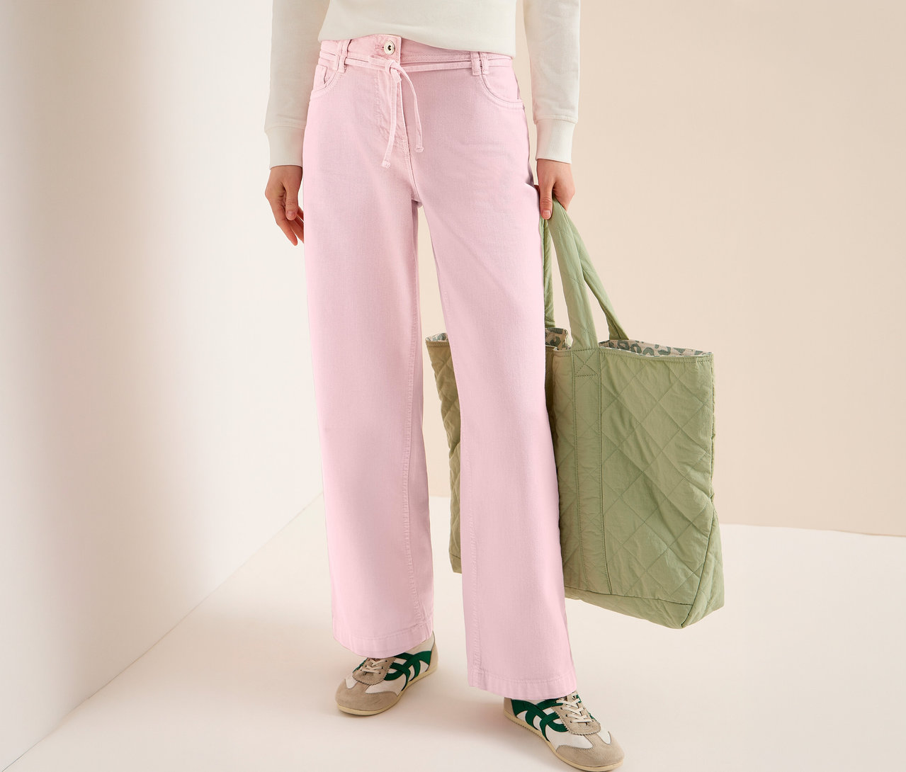 Une personne portant un jeans CECIL « Neele » rose, un sac en tissu vert et des baskets.