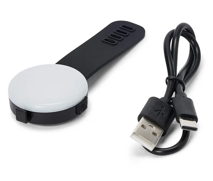 Une lumière LED noire et ronde avec une poignée noire et un câble USB reposent sur un fond blanc.