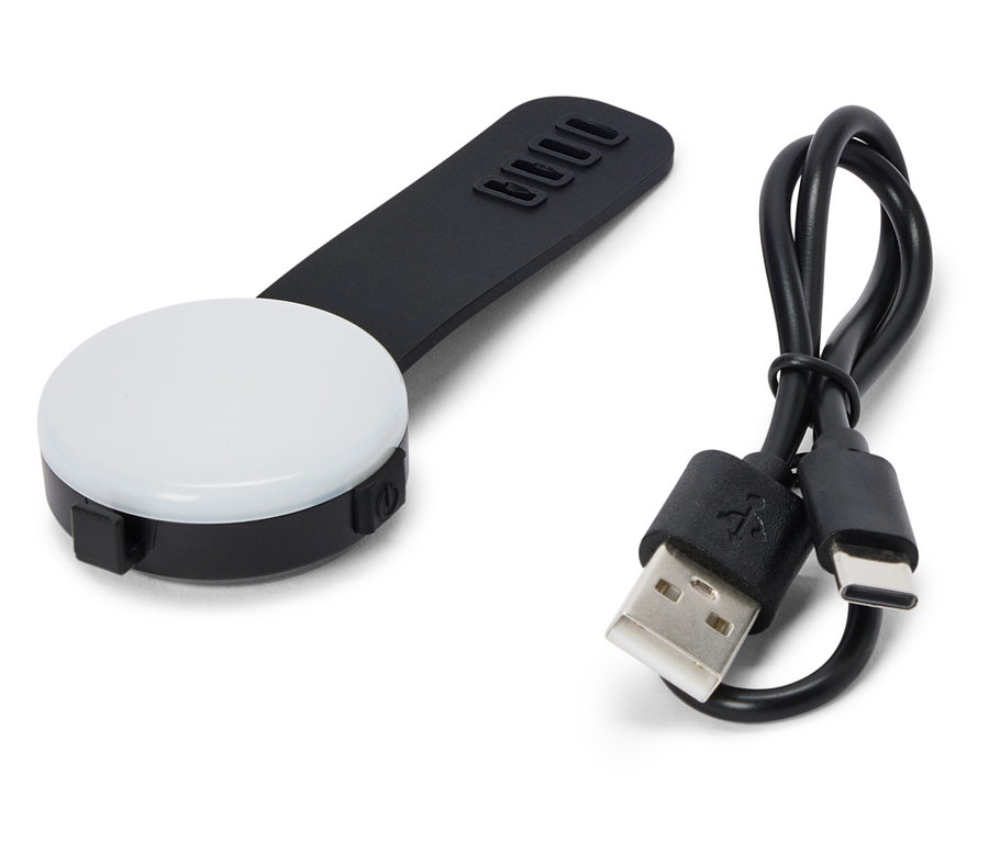 Une lumière LED noire et ronde avec une poignée noire et un câble USB reposent sur un fond blanc.