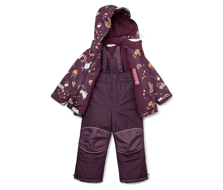 Une combinaison de ski violette pour enfant et une veste à motifs de licornes, d'étoiles et d'arcs-en-ciel sont posées sur le sol.