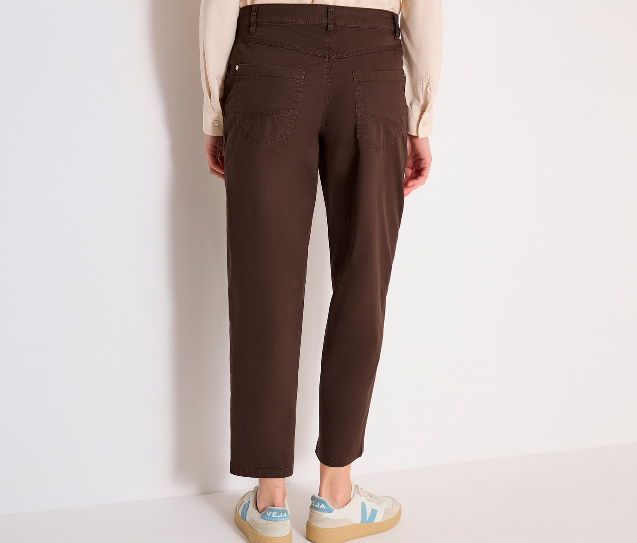 Une personne est debout, de dos, portant une chemise claire, un pantalon barrel CECIL « Scarlett » marron et des baskets claires.