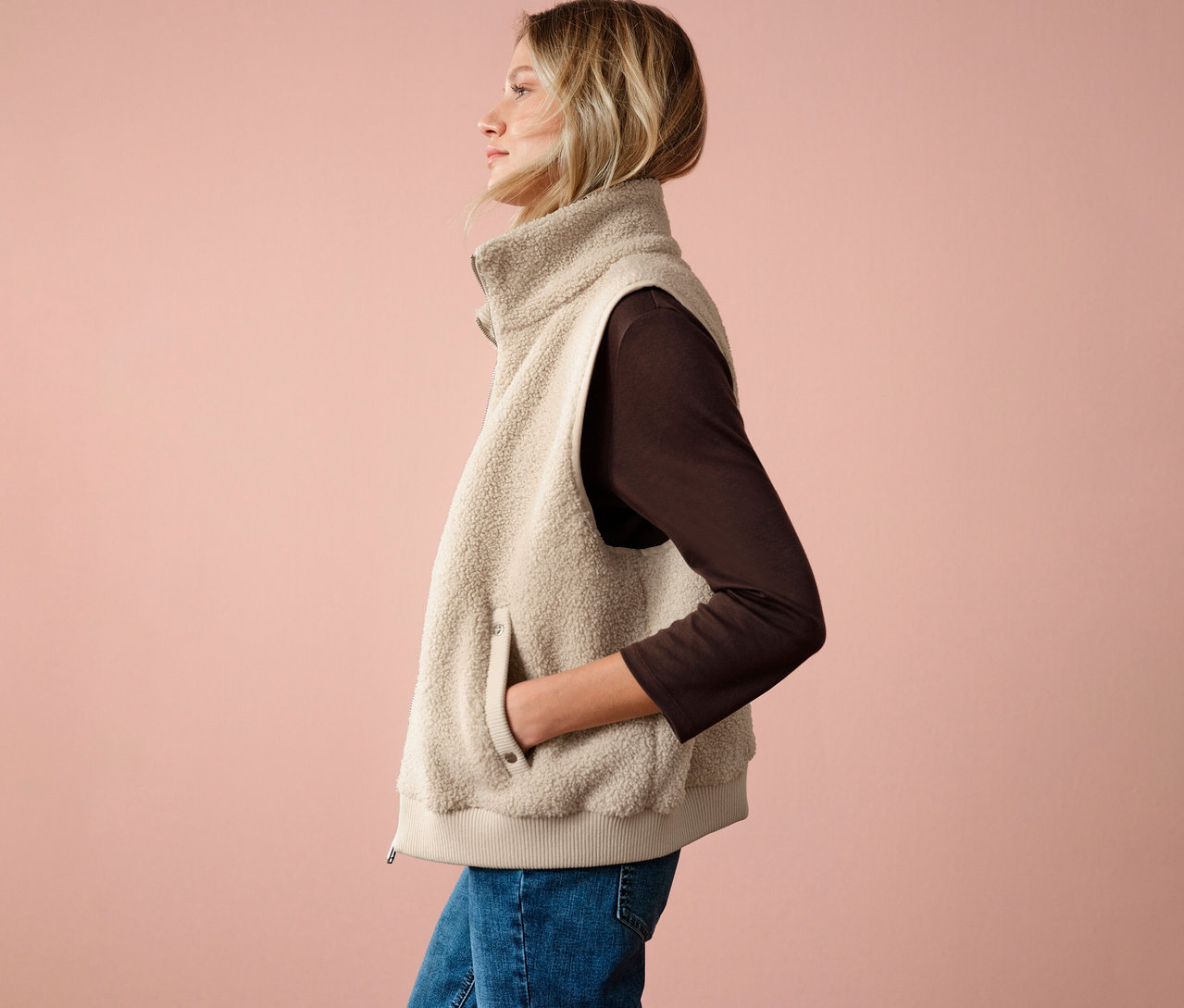 Femme portant une veste en teddy Street One, un haut marron et un jean, vue de côté sur un fond rose.