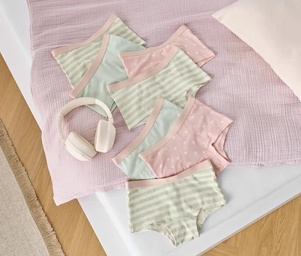 Sur un lit, des slips en coton à rayures et à étoiles sont posés à côté d'un casque blanc.