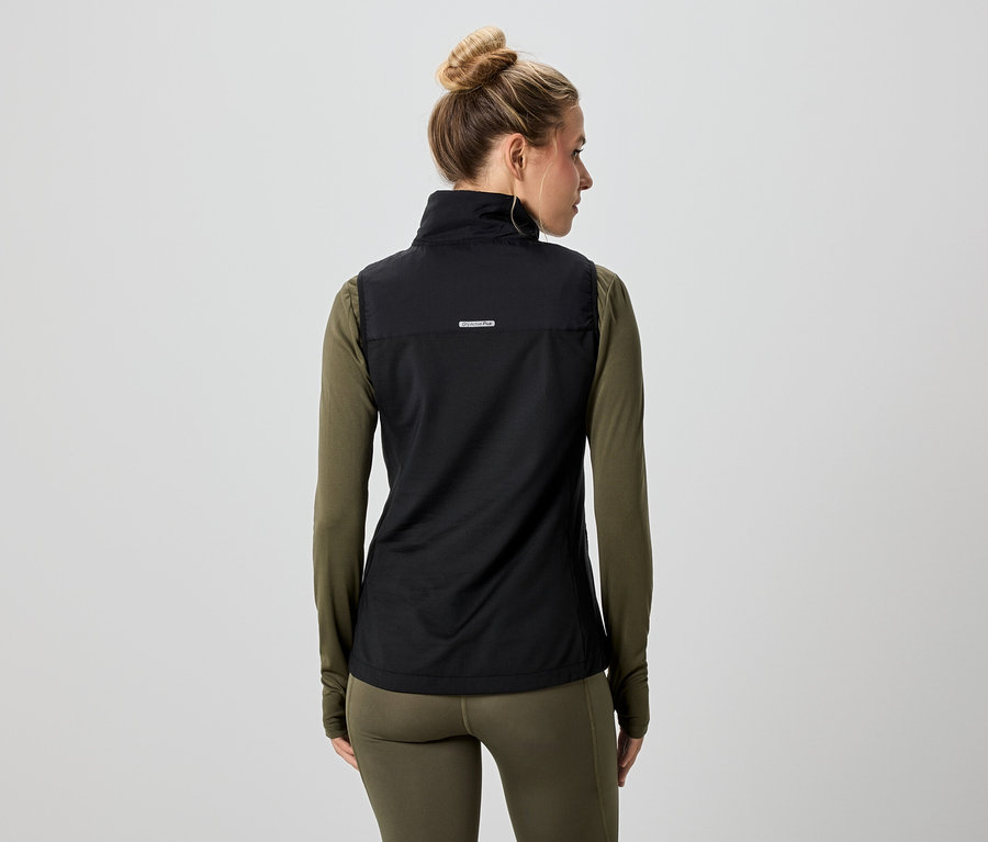 Vue arrière d'une femme portant un chignon, vêtue d'un gilet noir sur un t-shirt à manches longues et un legging vert olive.